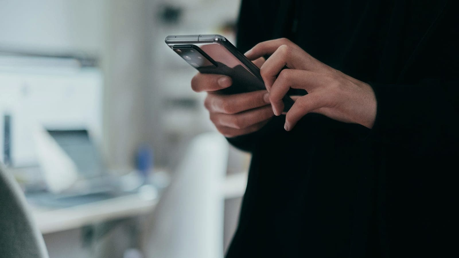 Pessoa digitando no celular em um escritório