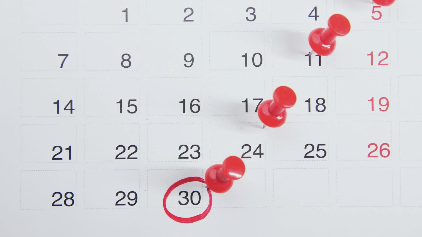 Calendário de parede com alfinetes vermelhos marcando datas